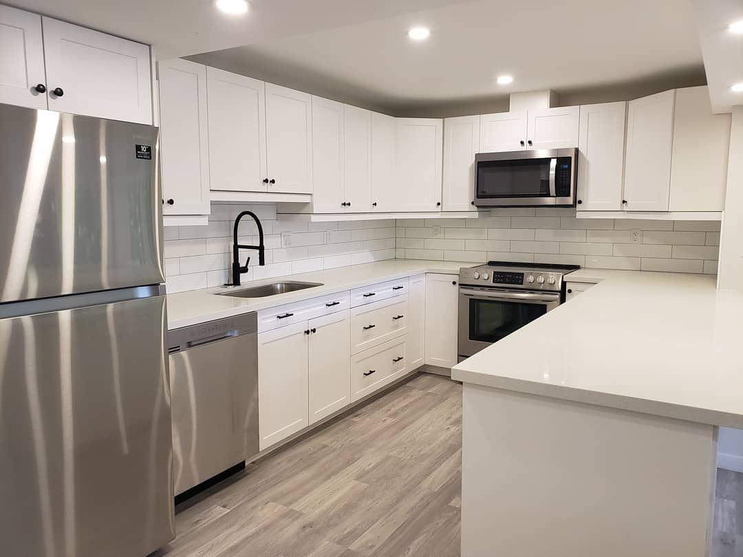 White kitchen with stainless steel appliances, black faucet, and subway tile backsplash.
